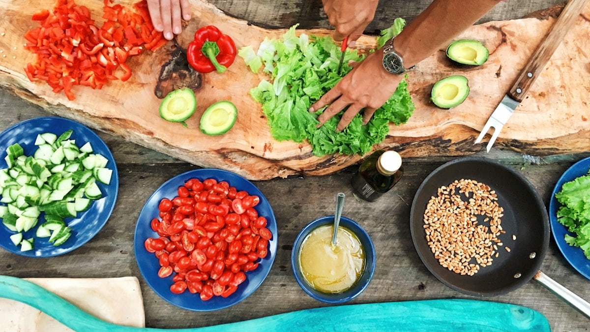 person slicing green vegetable in front of round ceramic plates with assorted sliced vegetables during daytime